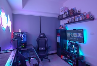 A modern gaming setup featuring a sleek gaming chair, dual monitors on a desk, and LED lighting. A gaming console and various decorations are displayed on shelves, creating an organized and vibrant gaming environment.