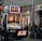 A collection of slot machines is situated inside a building with bright, colorful screens displaying various games and gaming themes. A person is seated nearby, seemingly relaxed with luggage beside them, and the atmosphere is lively with electronic displays.